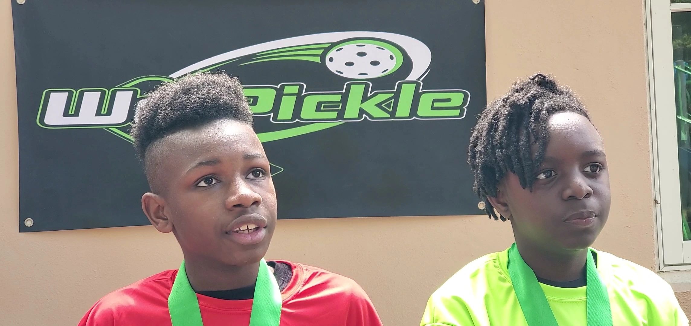 Two kids wearing pickleball medals indoors