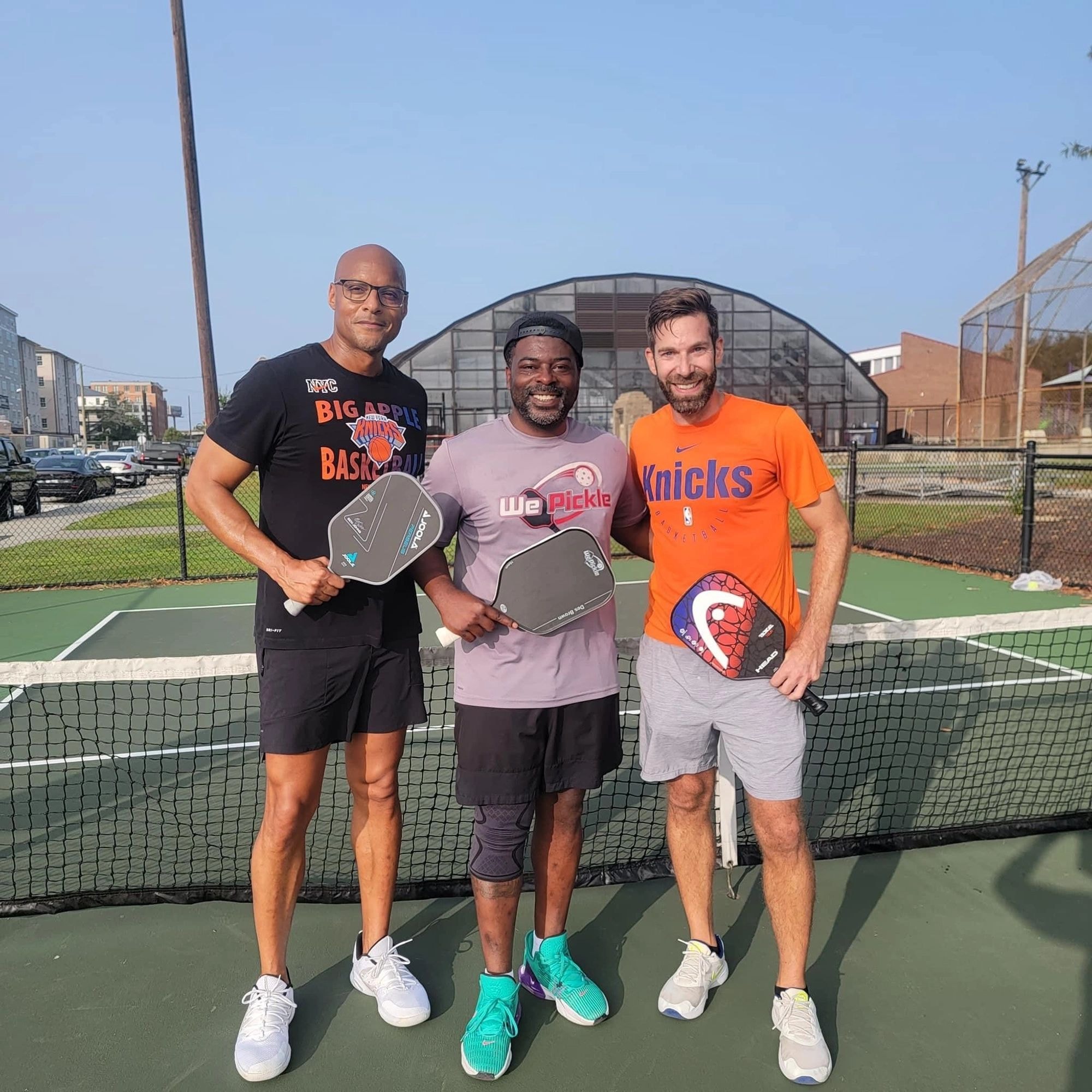 Three men holding pickleball paddles on court