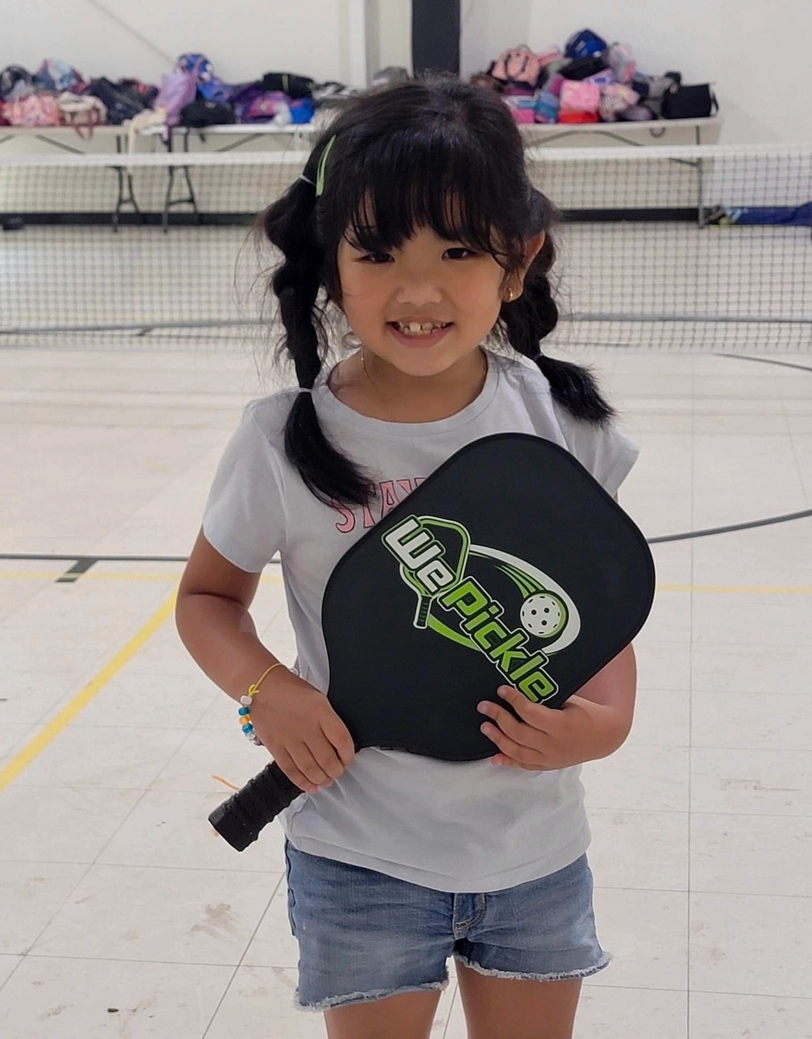 Young girl holding pickleball paddle indoors